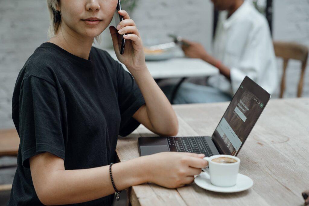 crop female talking on mobile phone with coffee and laptop